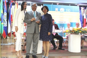 La directora del centro educativo, Lourdes Fabal Sosa, junto a Laura Herrera, secretaria general del Modelo Internacional de las Naciones Unidas del Colegio Santa Teresa, entregan una placa de reconocimiento a Evérgito Peña Acosta por su compromiso con la sostenibilidad y el medio ambiente. 